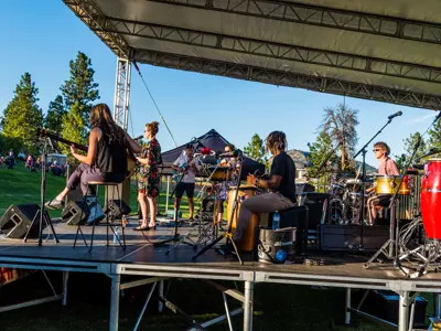 A six-person band performs for an outdoor crowd on a summer evening.