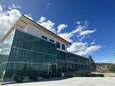 A view of a four-story city hall with clouds peaking past the roof in an otherwise clear summer sky.
