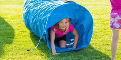 girl crawling through a blue fabric play tunnel in a park