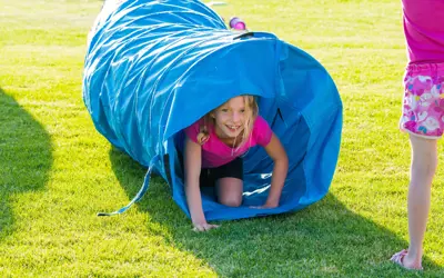 girl crawling through a blue fabric play tunnel in a park