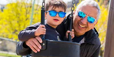 A happy father and son, who is on a swing, enjoy a day at the park.