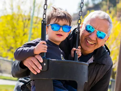 A happy father and son, who is on a swing, enjoy a day at the park.